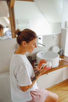 Beautiful woman taking care of skin by applying moisturizer cream in bathroom