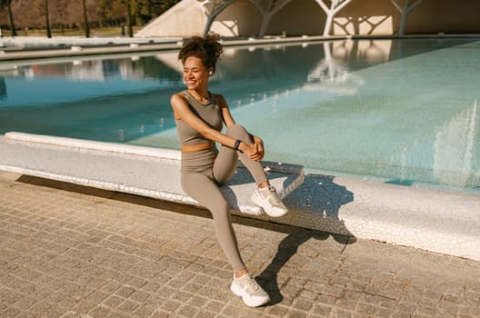 Smiling woman in sportswear have a rest after workout outside sitting on building background