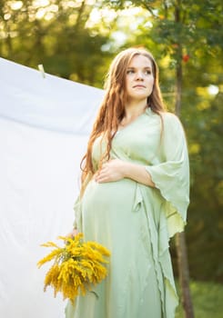 Pregnant woman with big belly, yellow Goldenrod Solidago flowers in hands. White female wears dress.Magic happy pregnancy. Childbirth preparations, emotional connection with baby. Baby shower Vertical