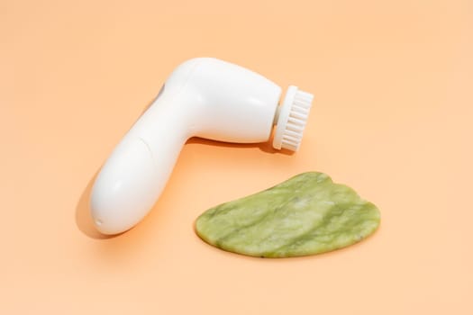 Closeup Skin Care Products. Facial Tool Gua Sha, Anti-Aging, Facial Cleansing Brush on Beige Background. Skin Beauty Device, Horizontal Plane. Nobody