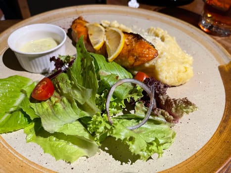 smoked grilled salmon fish served with salad and mash potatoes with lemons on top, served in plate perfect meal
