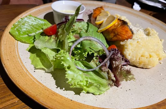 smoked grilled salmon fish served with salad and mash potatoes with lemons on top, served in plate perfect meal