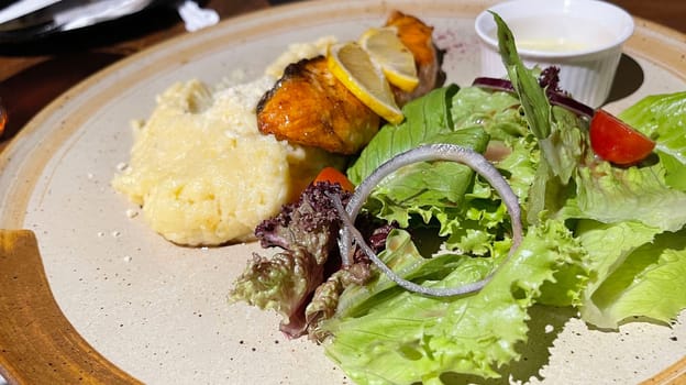 smoked grilled salmon fish served with salad and mash potatoes with lemons on top, served in plate perfect meal