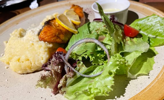 smoked grilled salmon fish served with salad and mash potatoes with lemons on top, served in plate perfect meal
