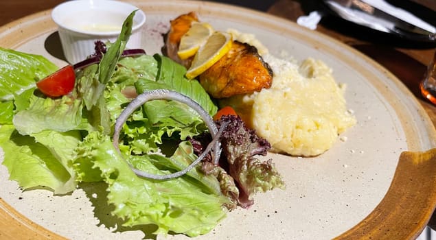 smoked grilled salmon fish served with salad and mash potatoes with lemons on top, served in plate perfect meal