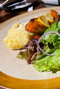 smoked grilled salmon fish served with salad and mash potatoes with lemons on top, served in plate perfect meal