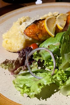 smoked grilled salmon fish served with salad and mash potatoes with lemons on top, served in plate perfect meal