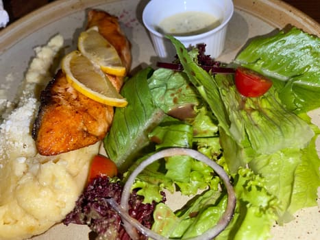 smoked grilled salmon fish served with salad and mash potatoes with lemons on top, served in plate perfect meal