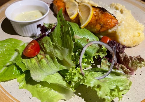 smoked grilled salmon fish served with salad and mash potatoes with lemons on top, served in plate perfect meal