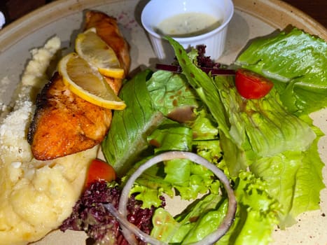 smoked grilled salmon fish served with salad and mash potatoes with lemons on top, served in plate perfect meal