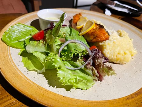 smoked grilled salmon fish served with salad and mash potatoes with lemons on top, served in plate perfect meal