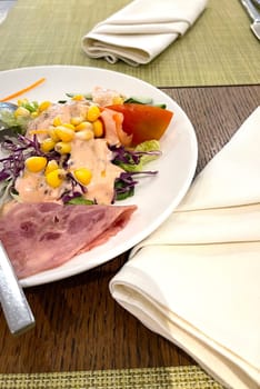 delicious breakfast, ham and fresh summer salad on white plate, on wooden table, view from above, good for your multimedia content background