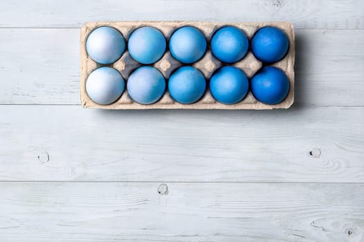 Easter concept. Ombre eggs in blue colors in cardboard packaging on neutral wooden background with copy space for text. Top down view or flat lay