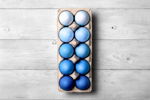 Easter concept. Ombre eggs in blue colors in cardboard packaging on neutral wooden background with copy space for text. Top down view or flat lay