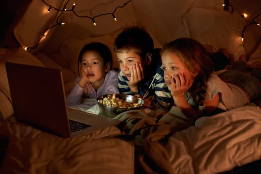 Children, laptop and watch in tent at night with movies, film or cartoons for holiday adventure or vacation. Young boy, girl or kids with lights, pillows and blanket at home on computer for Netflix.