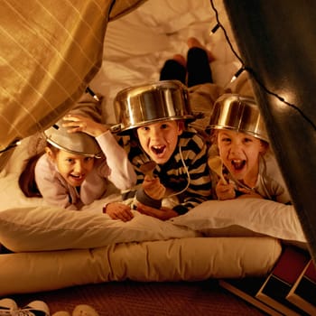 Children, portrait and siblings with pot helmet in a fort for fantasy, learning or playing in their home. Happy family, face and kids on a floor with tent games, development or fun bonding in a house.