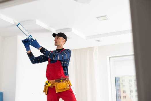 man plasterer construction worker at work, takes plaster from bucket and puts it on trowel to plastering the wall, wears helmet inside the building site of a house