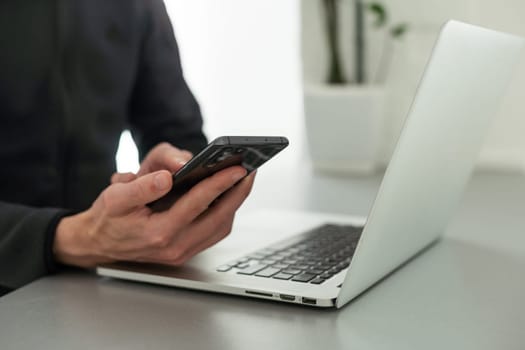 Hand holding smartphone and using laptop