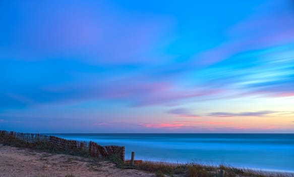 Sunset beach scene with a pink and blue sky, long exposure for silky water and fluffy clouds.