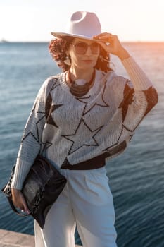 Stylish seashore woman. Fashionable woman in a white hat, white trousers and a light sweater with a black pattern on the background of the sea