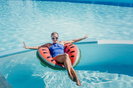 Happy woman in a swimsuit and sunglasses floating on an inflatable ring in the form of a watermelon, in the pool during summer holidays and vacations. Summer concept