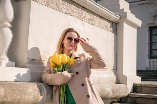 Woman holding yellow tulips, leaning against stone wall. Women's holiday concept, giving flowers