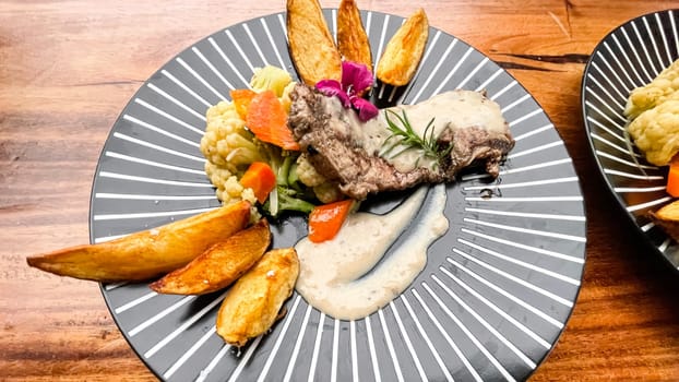 Juicy beef steak with salad and potato wedges along with pepper corn sauce served on black and white stripe on a wooden stone table. Top view