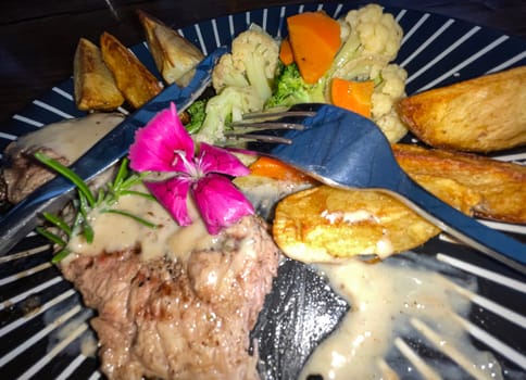 Juicy beef steak with salad and potato wedges along with pepper corn sauce served on black and white stripe on a wooden stone table. Top view