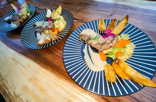 Juicy beef steak with salad and potato wedges along with pepper corn sauce served on black and white stripe on a wooden stone table. Top view