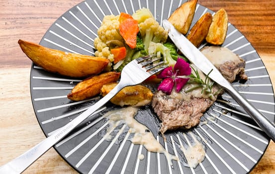 Juicy beef steak with salad and potato wedges along with pepper corn sauce served on black and white stripe on a wooden stone table. Top view