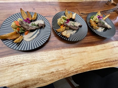 Juicy beef steak with salad and potato wedges along with pepper corn sauce served on black and white stripe on a wooden stone table. Top view