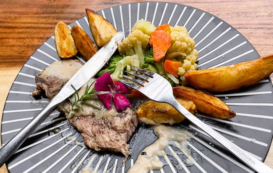 Juicy beef steak with salad and potato wedges along with pepper corn sauce served on black and white stripe on a wooden stone table. Top view