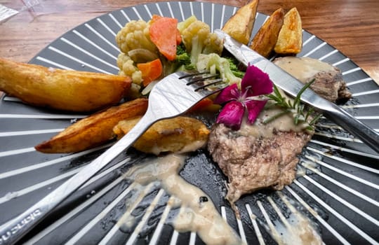 Juicy beef steak with salad and potato wedges along with pepper corn sauce served on black and white stripe on a wooden stone table. Top view