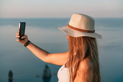 Selfie woman in hat, white tank top and shorts makes selfie shot mobile phone post photo social network outdoors on sea background beach people vacation lifestyle travel concept