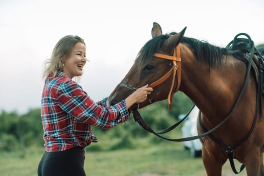 Happy blonde with horse in forest. Woman and a horse walking through the field during the day. Dressed in a plaid shirt and black leggings