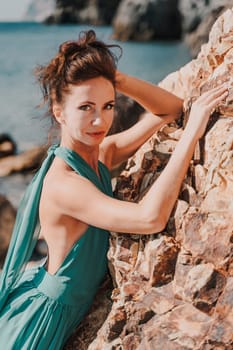 Woman green dress sea. Woman in a long mint dress posing on a beach with rocks on sunny day. Girl on the nature on blue sky background