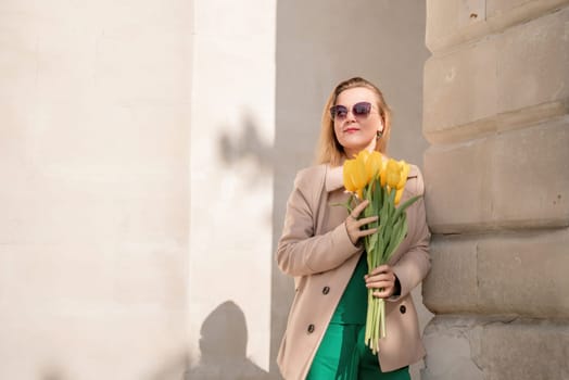 Woman holding yellow tulips, leaning against stone wall. Women's holiday concept, giving flowers