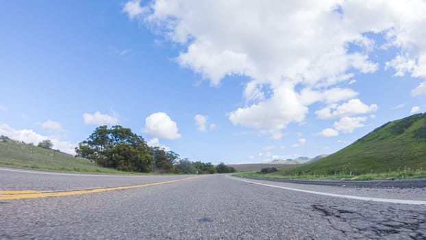 On a clear winter day, a car smoothly travels along Highway 101 near Santa Maria, California, under a brilliant blue sky, surrounded by a blend of greenery and golden hues.