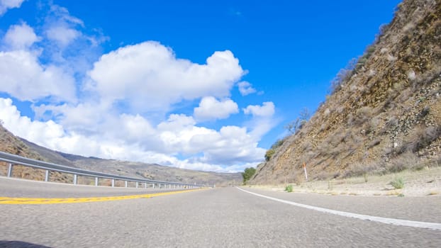 Vehicle is cruising along the Cuyama Highway under the bright sun. The surrounding landscape is illuminated by the radiant sunshine, creating a picturesque and inviting scene as the car travels through this captivating area.