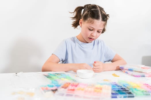 Little girl enjoys crafting colorful bracelets with vibrant clay beads set.