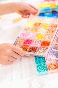 Little girl enjoys crafting colorful bracelets with vibrant clay beads set.