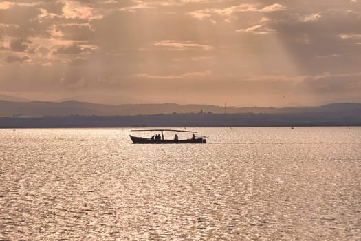 Silhouette of a boat full of people in the Albufera of Valencia. Sunset, sun, calm waters, tradition of reeds.