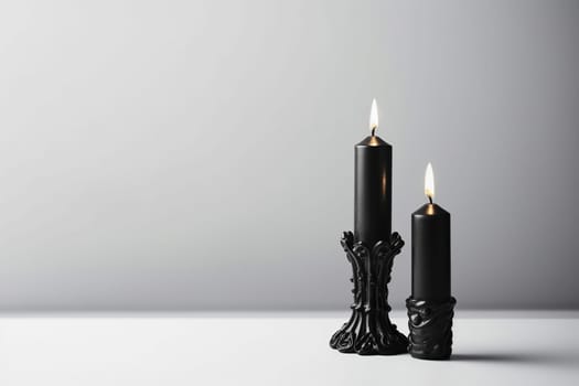 Two lit black candles in ornate holders against a gray backdrop.