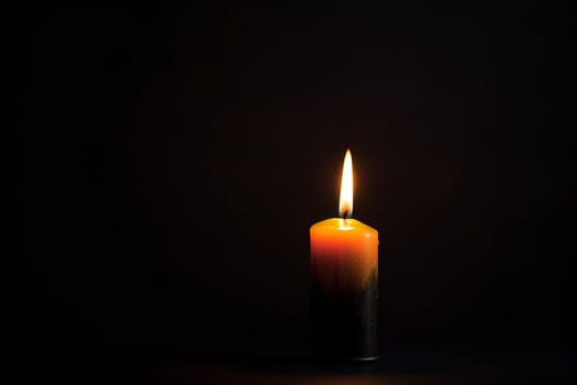 A lone lit candle against a dark background.