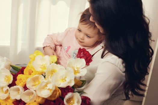 Cute little baby daughter and mom with flowers tulips. Mother and child hugging. Happy mother's day.