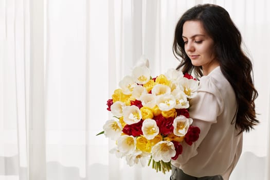 Beautiful woman in the white shirt with spring flowers tulips in hands. Women's Day