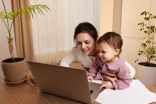 pretty businesswoman working at the computer with her little child girl at home