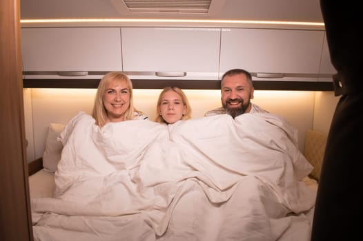 The family is getting ready for bed sitting on the bed in their motorhome.