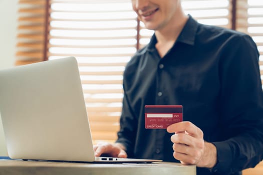 Young man using laptop with credit card for internet banking, online shopping E commerce by online payment gateway at home office. Modern and convenience online purchasing with debit card. Unveiling