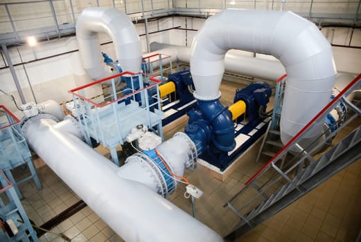 The industrial water pumping station features well-maintained pumps, pipes, and valves, brightly lit and showcasing precise engineering in efficient water management.